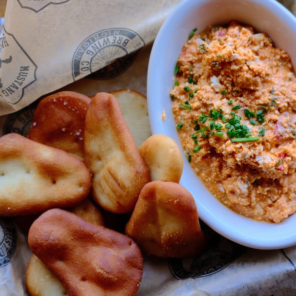 Pimento cheese dip with chives and pretzel bites on branded Mustang Lounge paper.