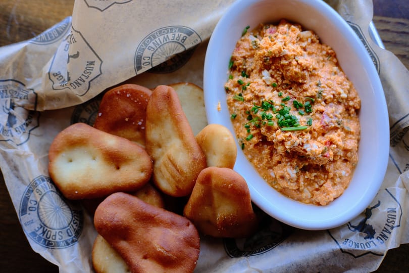 Pimento cheese dip with chives and pretzel bites on branded Mustang Lounge paper.