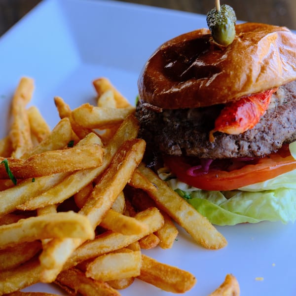 Gourmet burger with lobster, lettuce, tomato, and fries on a white plate.