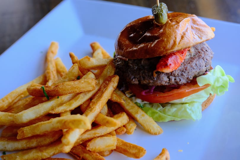 Gourmet burger with lobster, lettuce, tomato, and fries on a white plate.